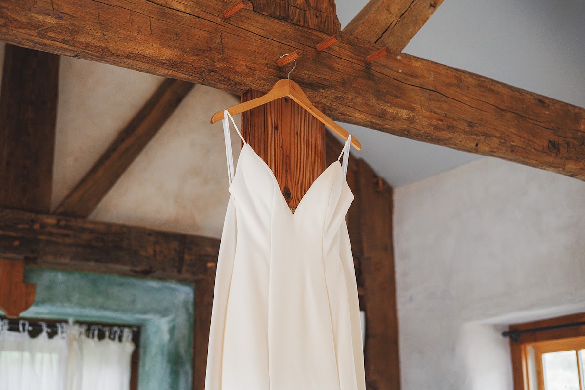 Amie's white wedding dress on a wooden hanger suspended from a rough-hewn timber beam in a whitewashed room at Zigbone Farm Retreat
