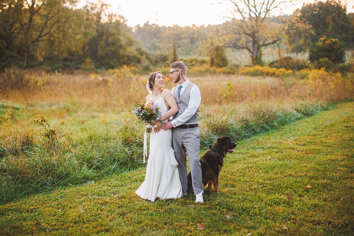 Amie and Cody embracing in the golden autumn meadow at dusk with Cujo standing beside them