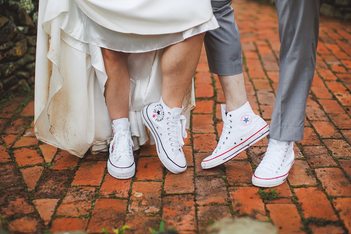 A couple's matching white Converse sneakers worn under their wedding attire