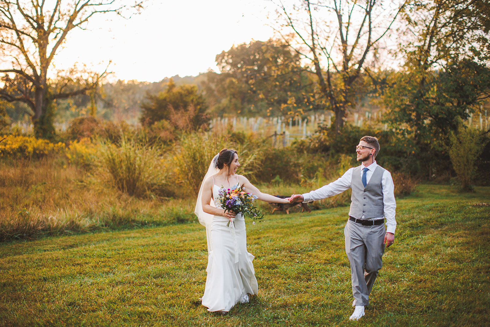 Cody leading Amie by the hand through a golden meadow at sunset at Zigbone Farm Retreat, low light raking across the tall grass