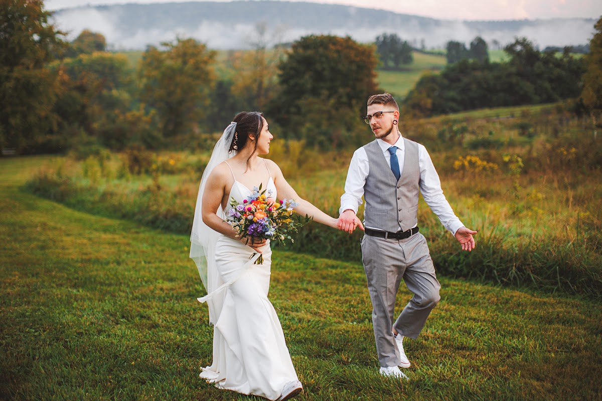 Amie leading Cody by the hand across the grass with mist hanging over the wooded hills behind them and a soft pastel sky above