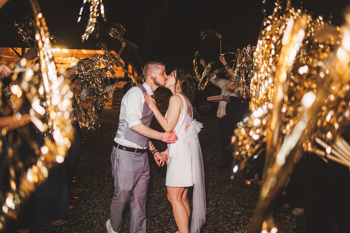 Amie and Cody kissing at night in a tunnel of gold streamers held aloft by guests lining the path