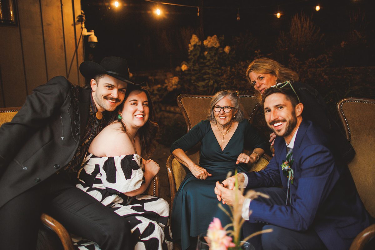 Guests settled into armchairs in the outdoor lounge at night under strings of lights, all of them laughing toward the camera