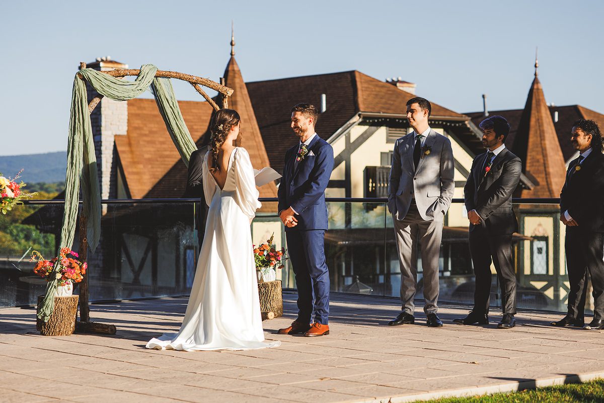 Andrea reading her vows to Patrick beneath the arch, the turreted Bavarian Inn chalets rising behind them