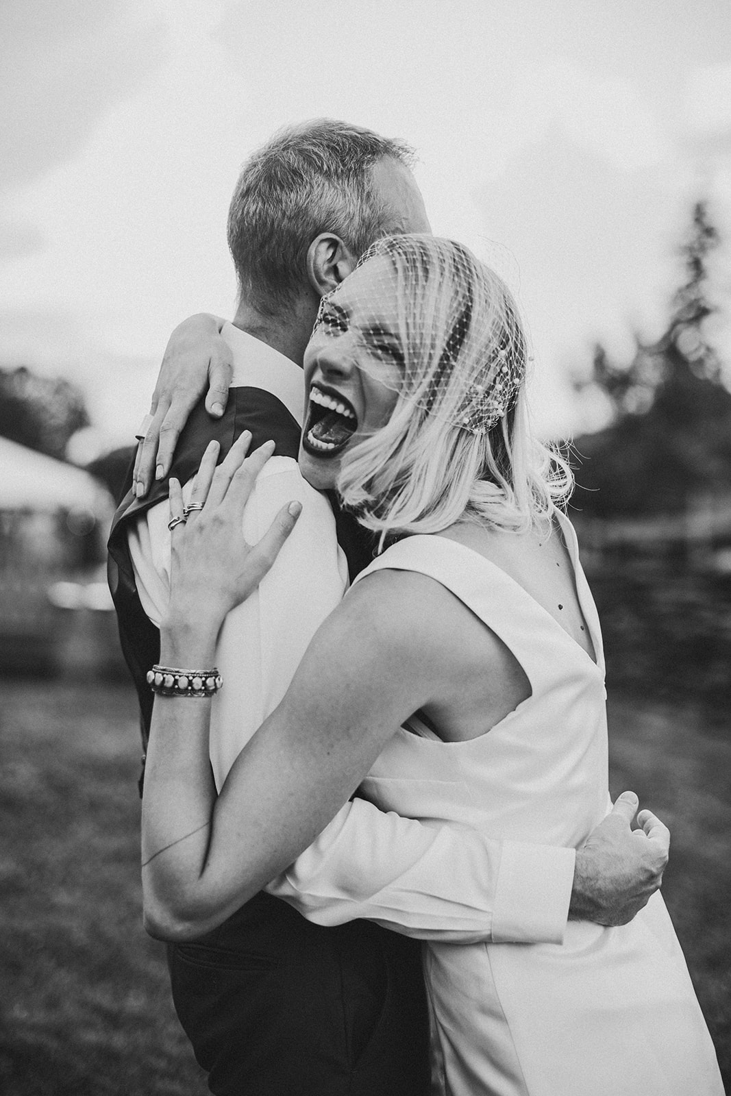 A black and white frame of a bride laughing wide open over the groom's shoulder mid-embrace