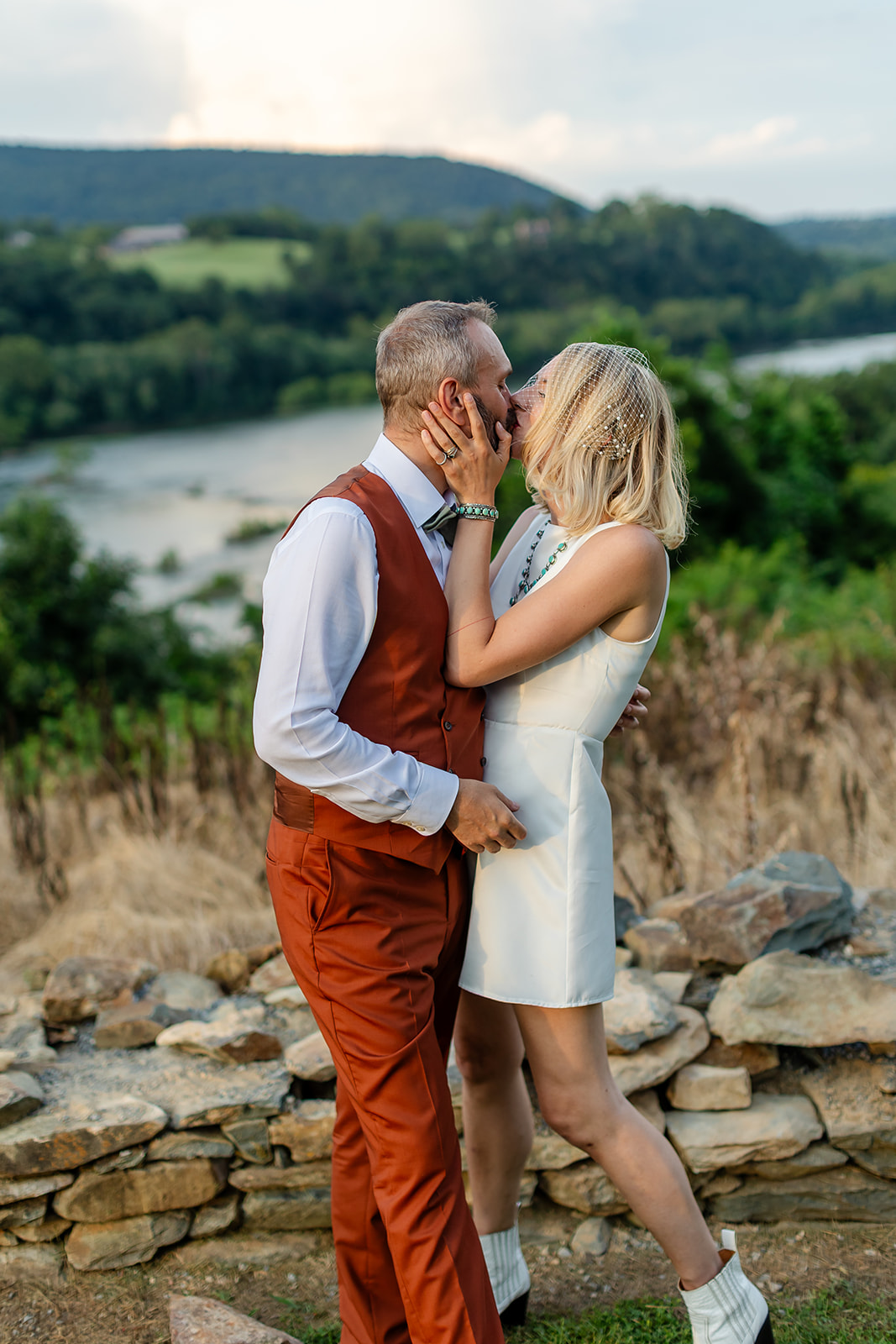Annie and Thomas kissing at the stone wall, her hand on his cheek, the river and green farmland stretching into the distance