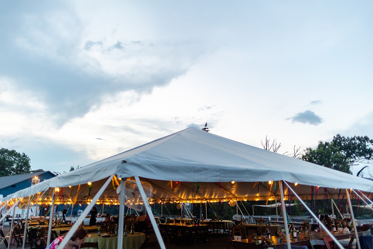 The reception tent at Harpers Ferry Brewing glowing with string lights under a dusk sky, tables set on the lawn beneath it