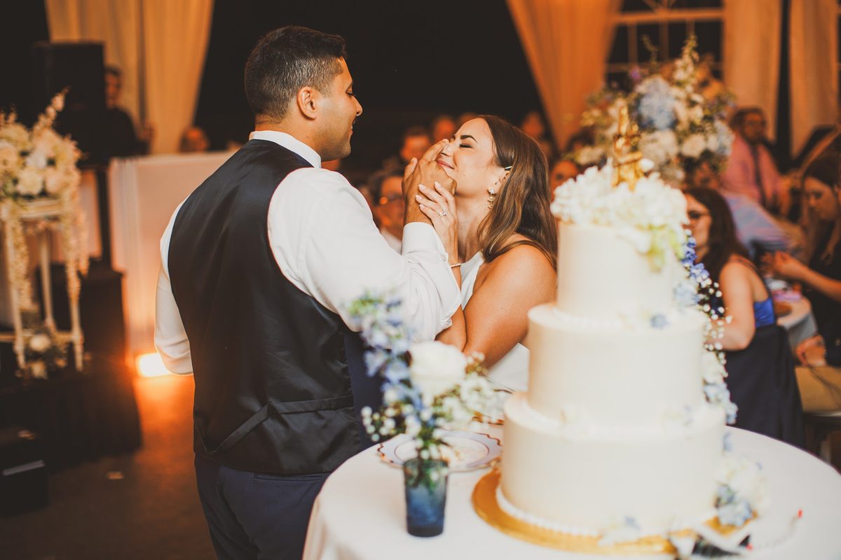 Youssef holding his hand to Bailey's cheek as she laughs through the first bite of cake beside the three-tier cake