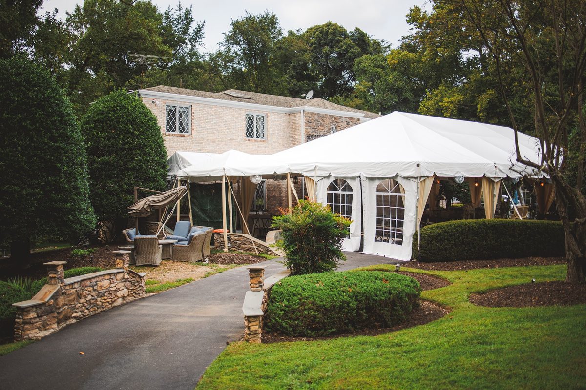 The brick and stone house at the Brinklow estate with leaded windows, boxwood hedges, and the white reception tent wrapping the lawn