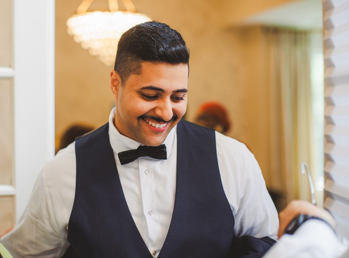 Youssef smiling down in a navy vest and black bow tie while getting ready beneath a chandelier