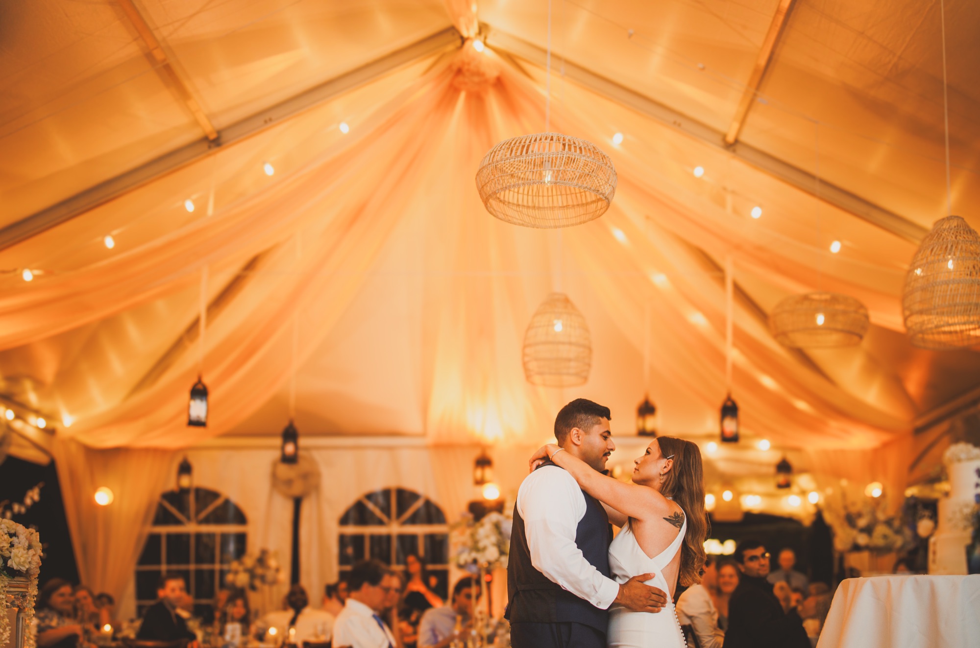 A couple during their first dance beneath a glowing, warmly draped reception tent