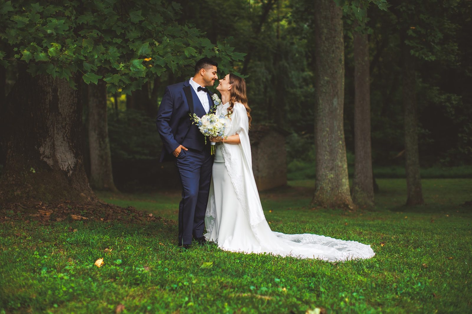 A couple nose to nose with the bouquet held between them in soft green woodland light