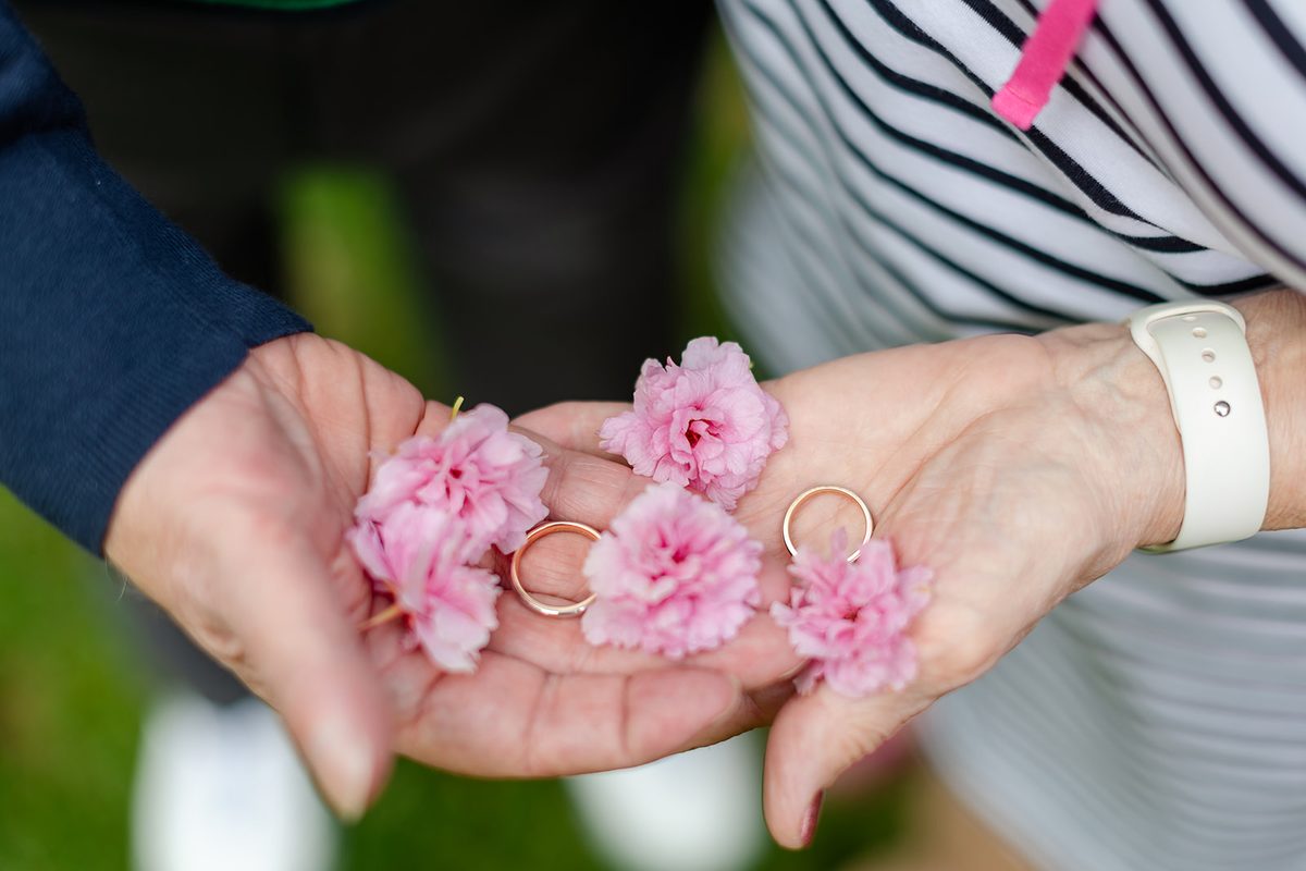 Two gold wedding bands resting in a cluster of pale pink cherry blossoms held in Mary's hand