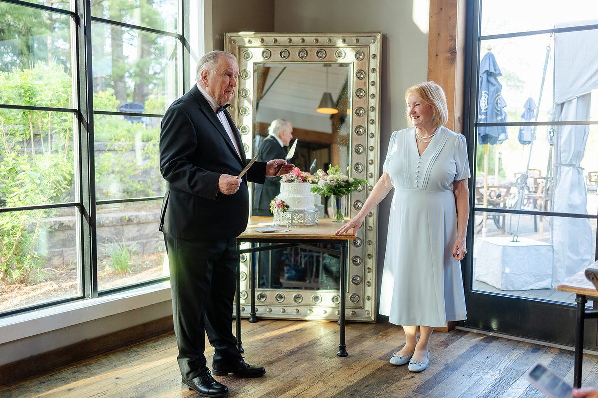 Mary and Mark cutting their wedding cake together in front of a large gilt mirror