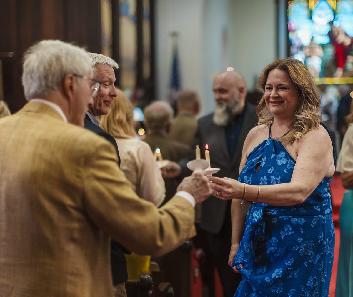Guests in the pews leaning toward one another to pass a candle flame down the row