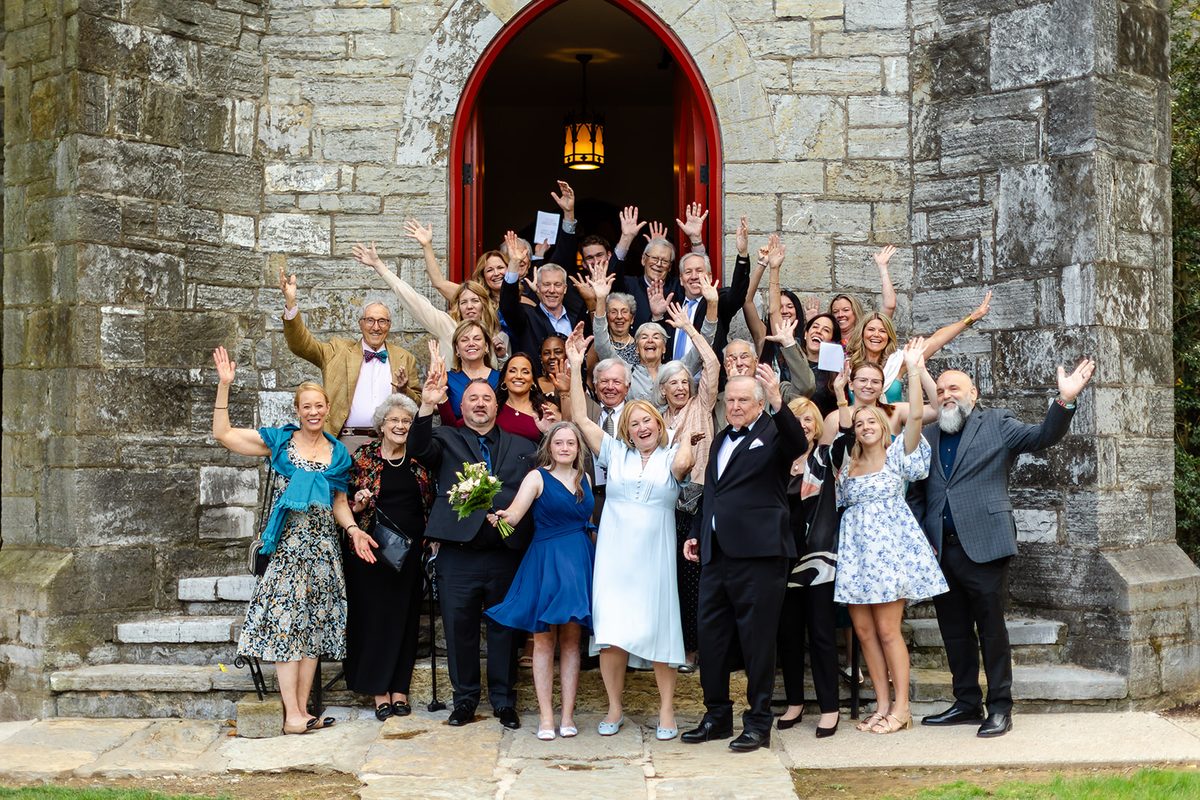 A wedding party cheering with arms raised on the stone steps in front of a Gothic church