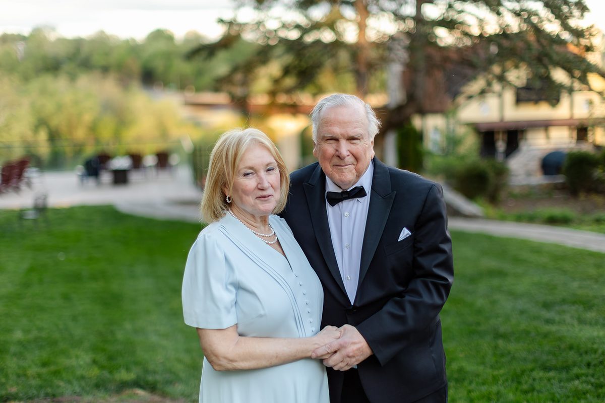 Mary and Mark standing together in golden evening light on the Bavarian Inn lawn, the Potomac valley soft behind them