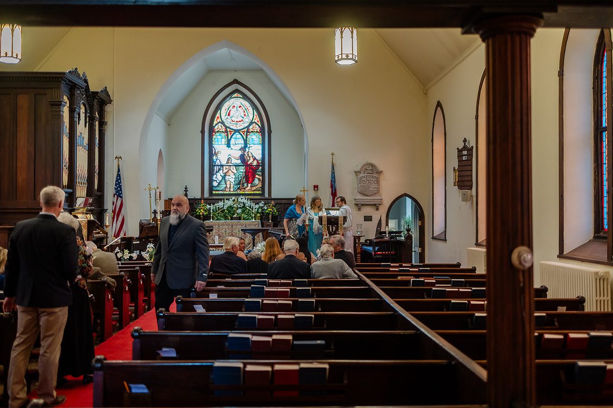 The nave of Trinity Episcopal Church filled with seated guests, sunlight through stained glass and Easter lilies at the chancel