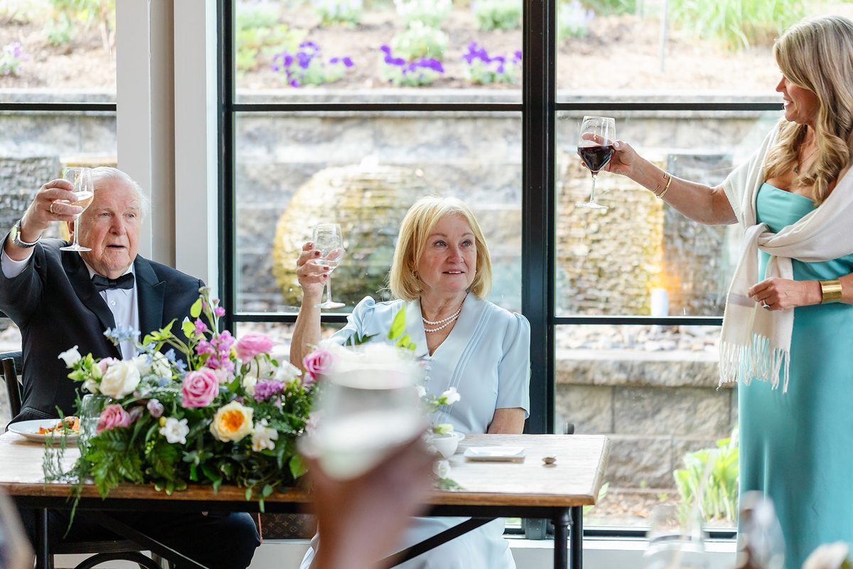 Mary and Mark laughing and raising glasses at their table during the toasts