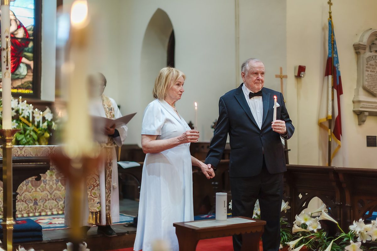Mary and Mark holding lit taper candles and each other's hands at the chancel