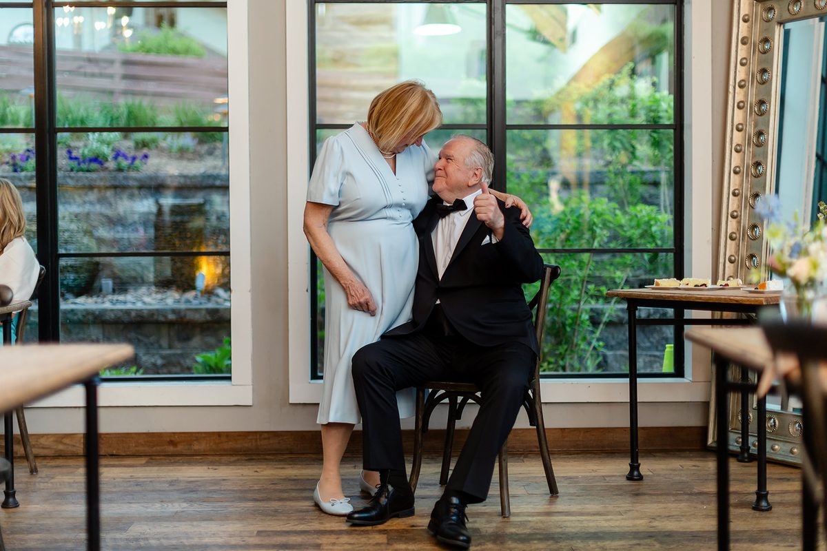 Mary with her arm around Mark by the window at the Bavarian Inn as he gives a thumbs up, both laughing