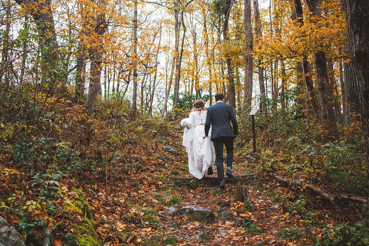 A couple walking hand in hand up a leaf-covered trail through golden autumn woods