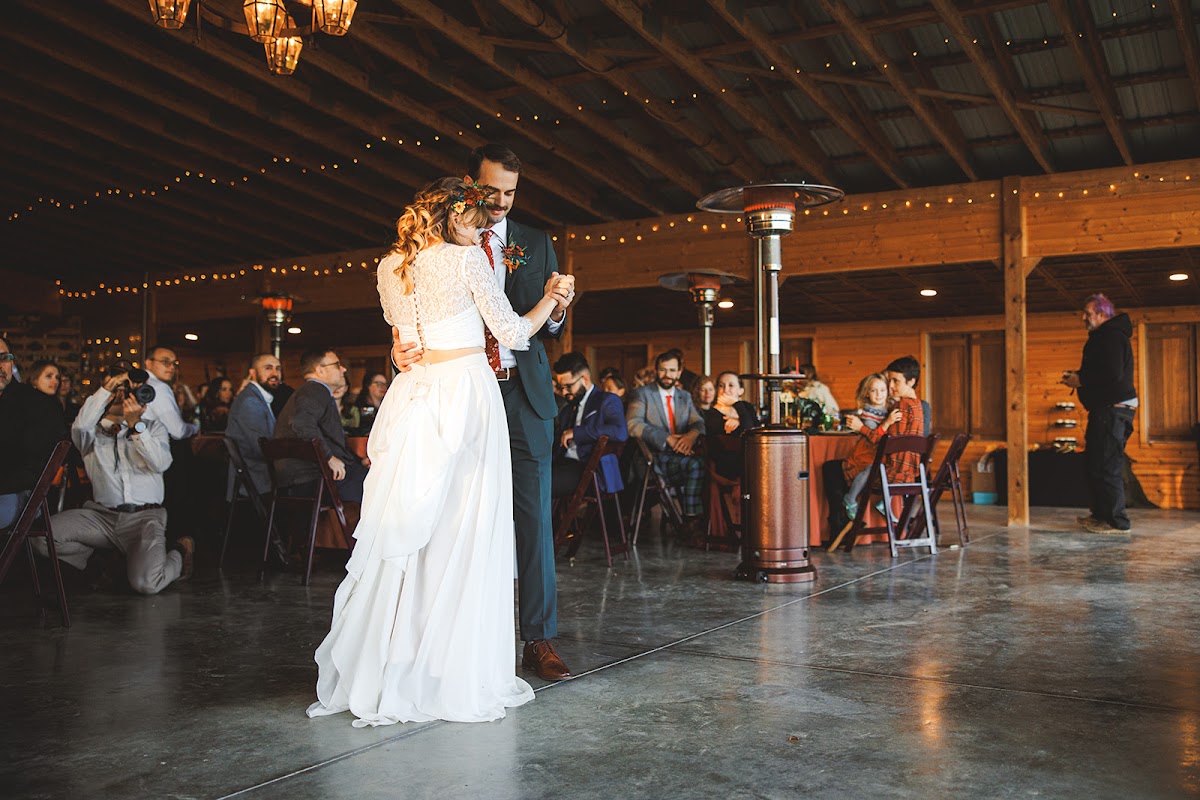 Sara and Ryan's first dance on the concrete floor of the string-lit barn at River's Bend Ranch, guests watching from tables along the walls