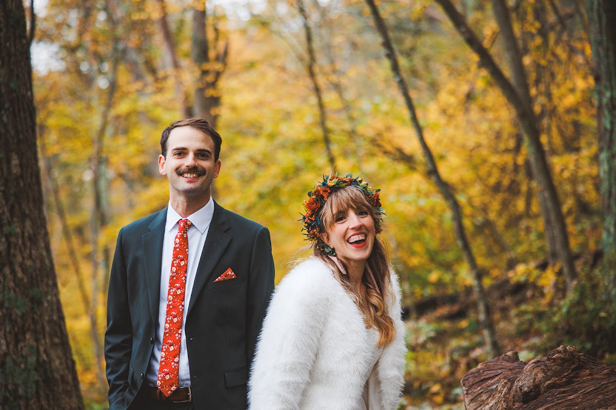 A couple standing together in bright yellow autumn woods, the bride laughing in a white fur coat