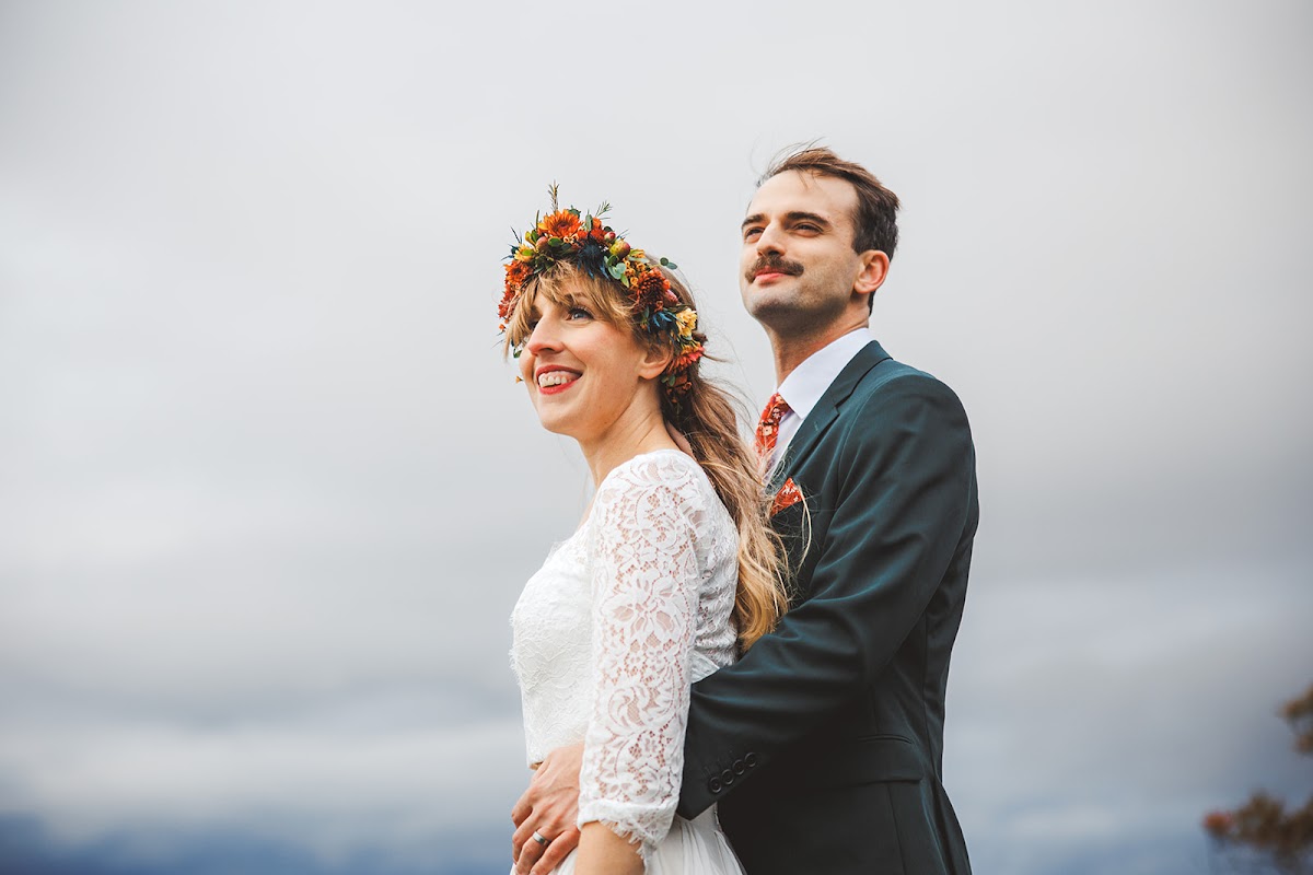 Sara and Ryan looking out from the overlook together, wind in her hair, his arms around her waist against the gray sky