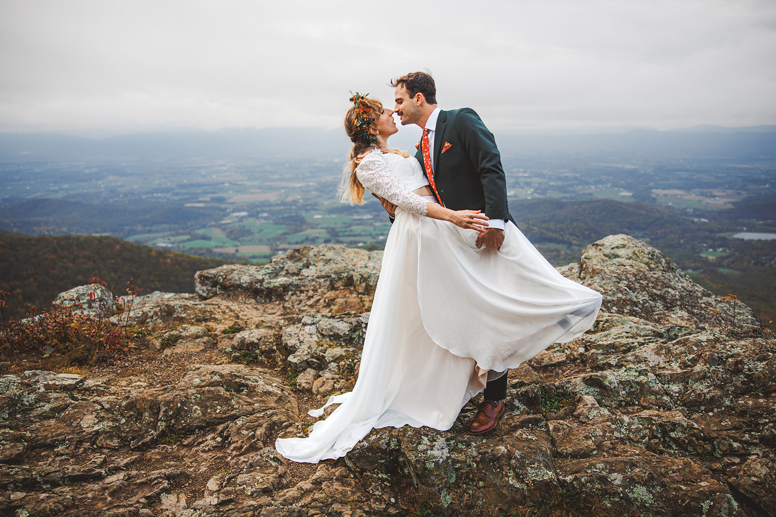 Ryan pulling Sara into a kiss on a rock outcrop above the autumn Shenandoah Valley, her white skirt lifting in the wind