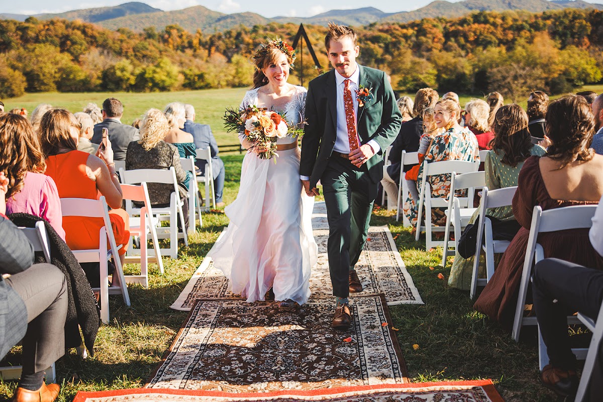 Sara and Ryan walking back up the aisle of layered vintage rugs hand in hand, the triangle arch and autumn mountains behind them