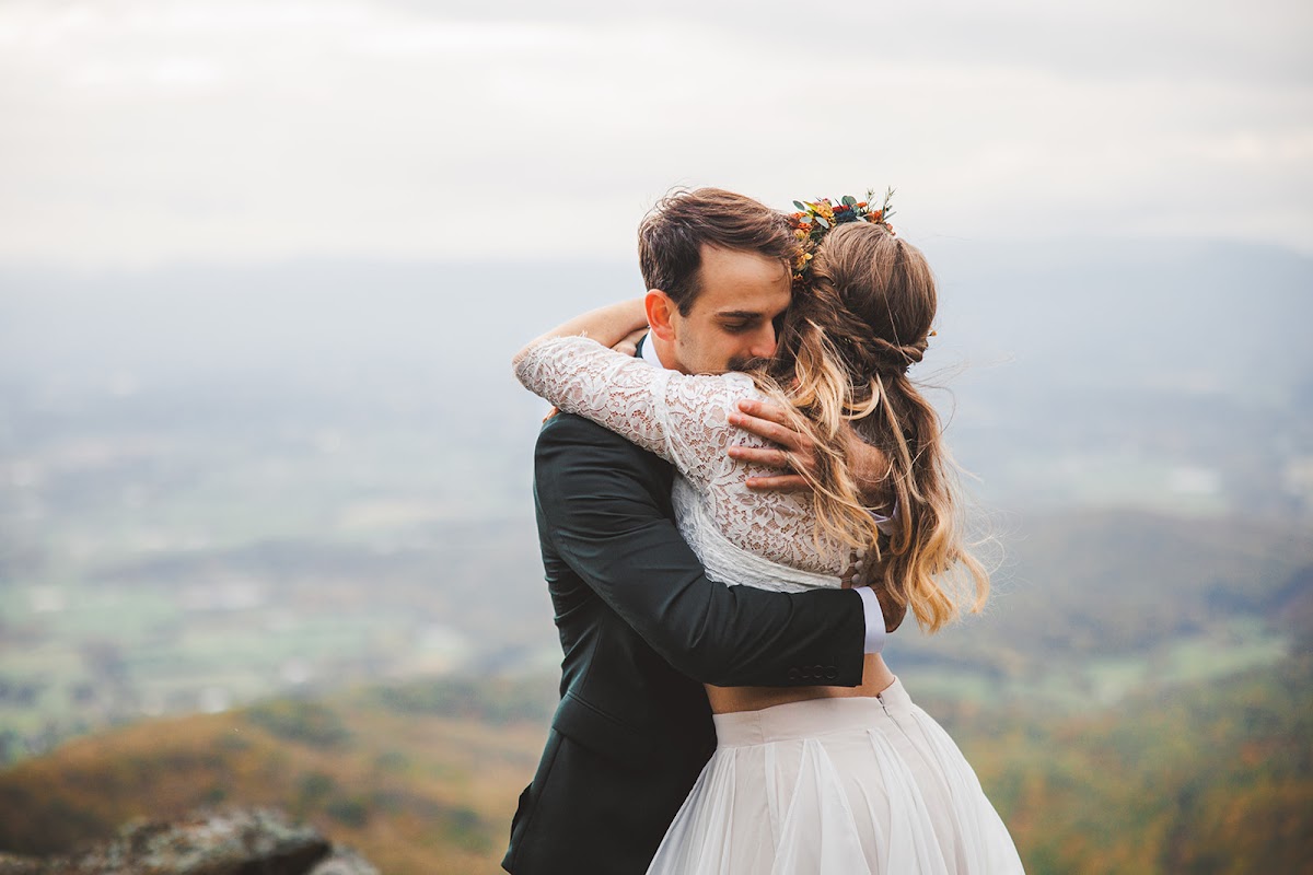 A couple holding each other tightly on a summit, the valley soft and out of focus behind them