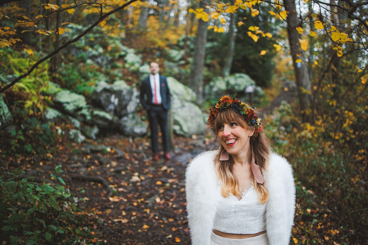 A bride in an autumn flower crown laughing on the trail as the groom waits behind her