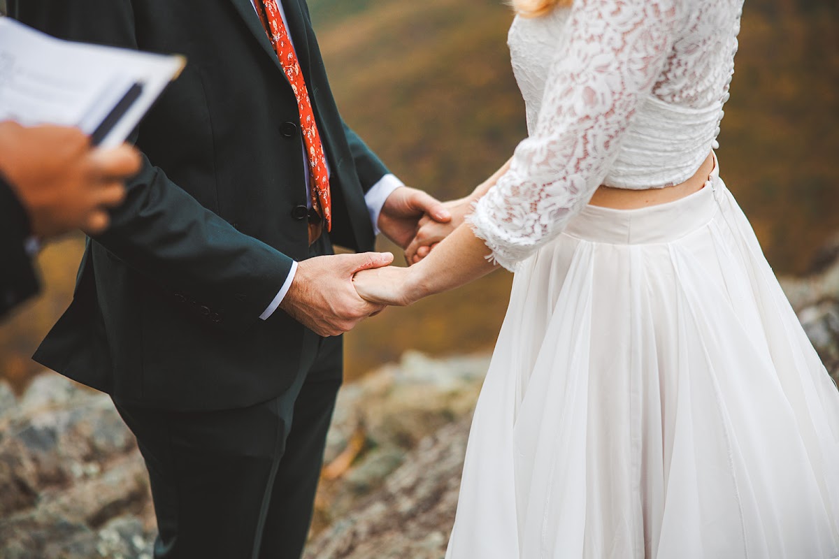 A close frame of a couple holding hands during their vows, the officiant's book just in view