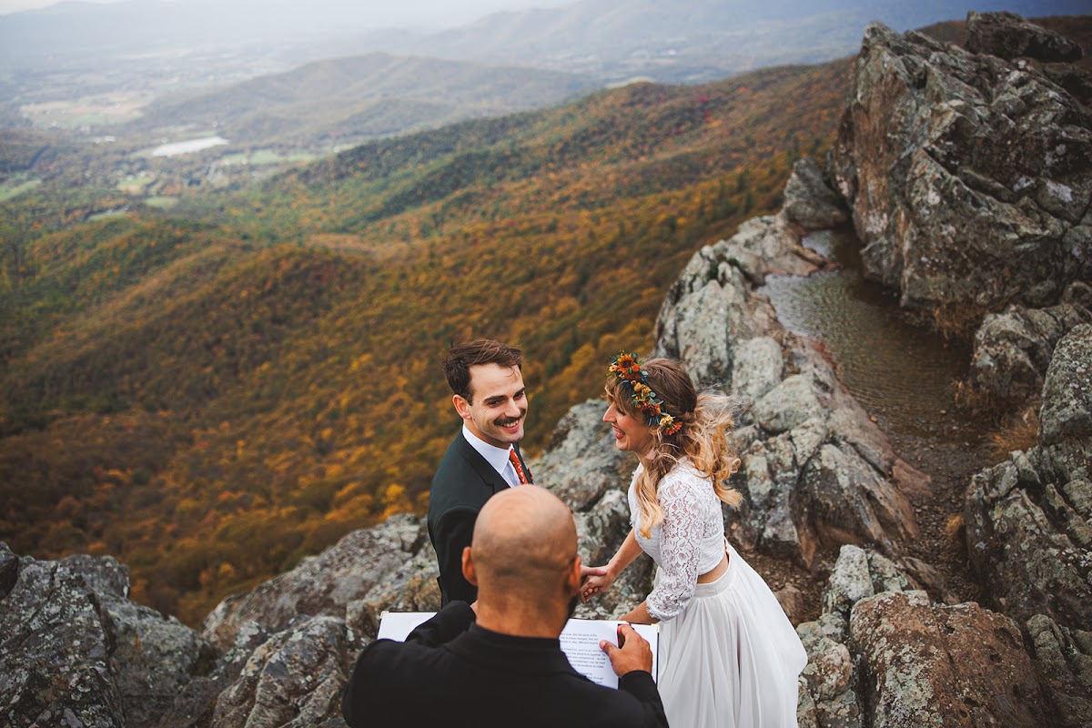 A couple reading vows on a rocky summit with autumn ridges falling away behind them