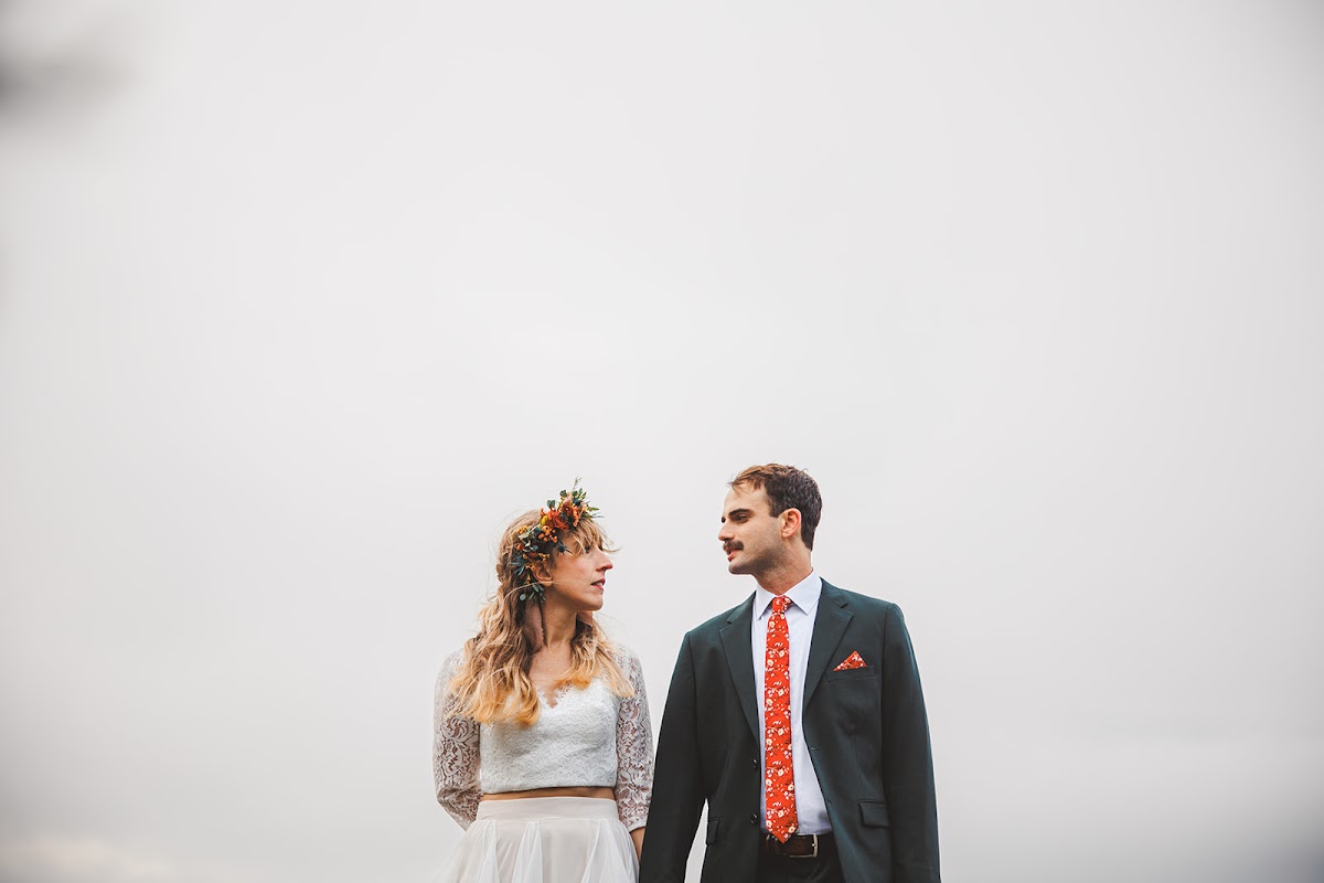 A couple standing side by side against a blank white overcast sky, turned to look at each other