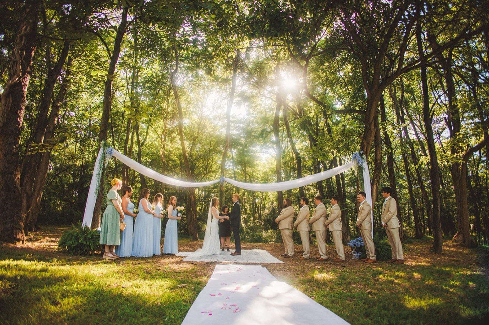 Claire and Evan's ceremony in the woods, sun breaking through the canopy