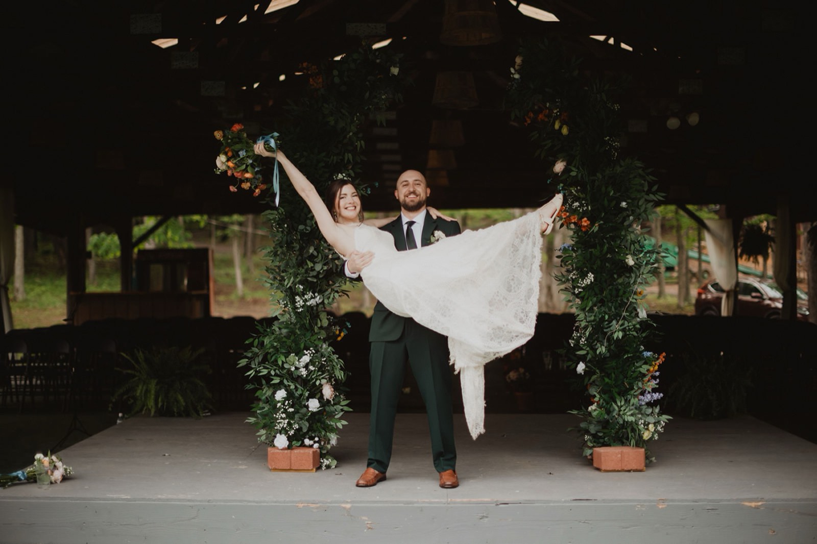 Emily lifted in Garrett's arms beneath their floral ceremony arch at Coolfont Resort