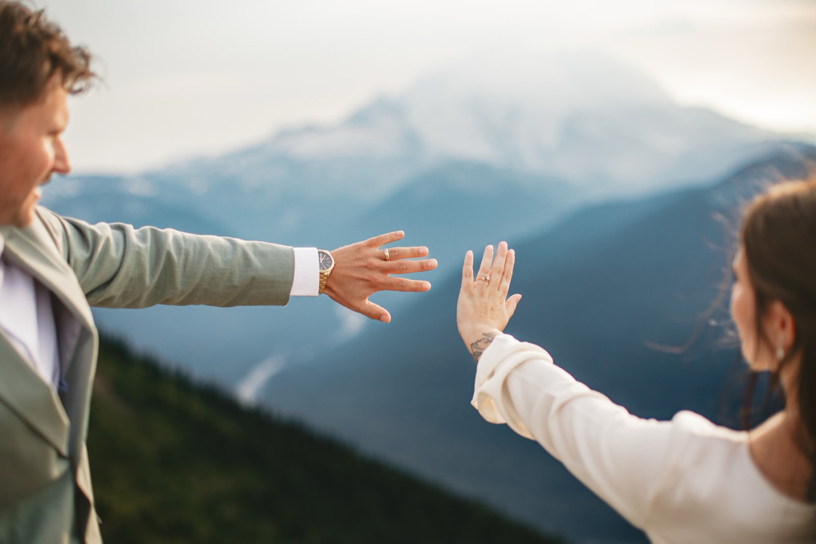 Michaela and AJ reaching their ringed hands toward each other, Mount Rainier behind them