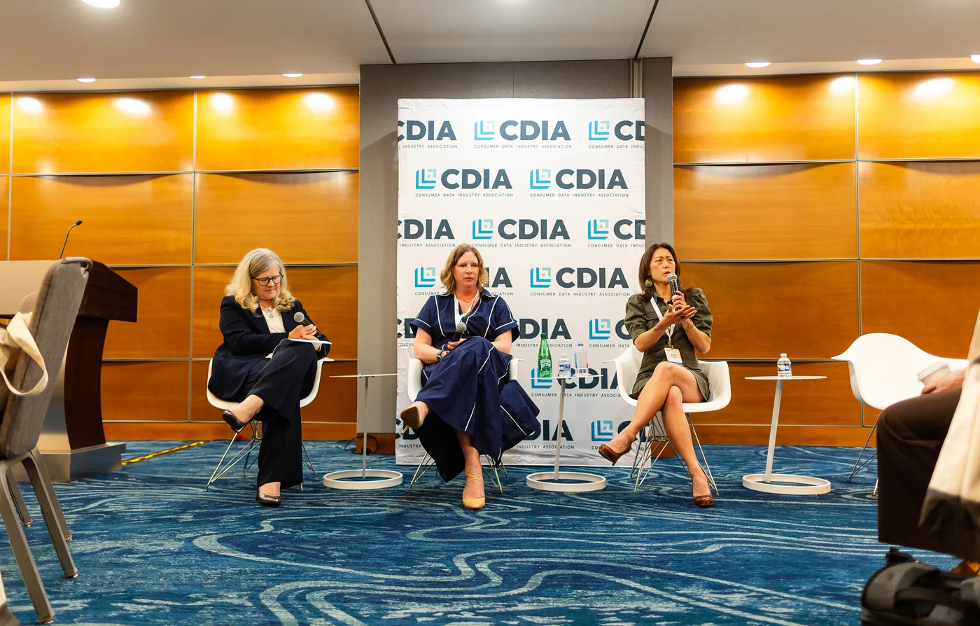 Three panelists seated on a stage in front of a CDIA logo wall, with a blue carpet in the foreground.