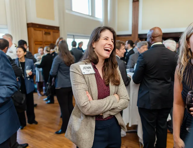 Woman laughing mid-conversation in a busy reception.