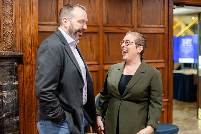 Two people mid-laugh against the wood paneling.