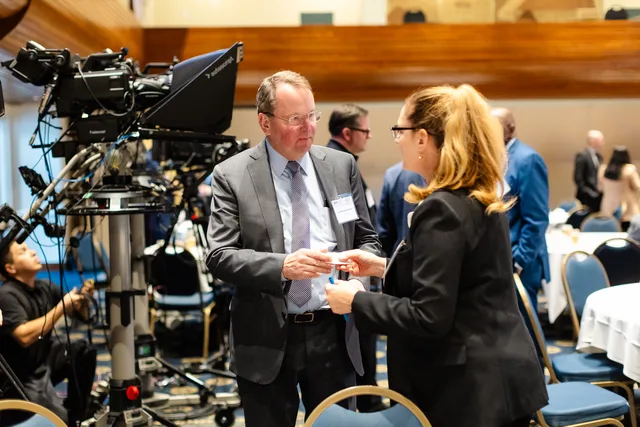 Two people exchanging cards in front of TV camera rig.