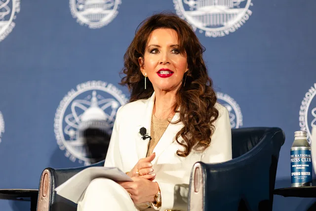 Moderator in white seated against a blue seal backdrop.