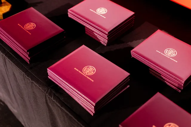 Stacks of maroon diploma covers on a dark table.