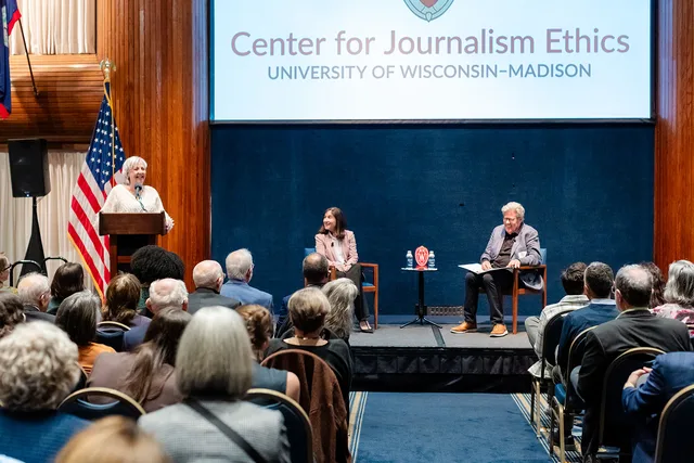 Moderator at the podium and two seated speakers on stage, with the audience in the foreground.