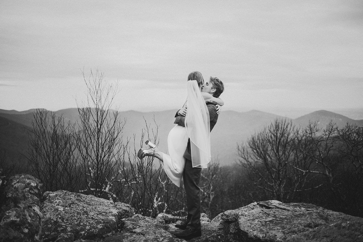 A groom lifting his bride into a kiss on a rocky ridge with distant mountains behind