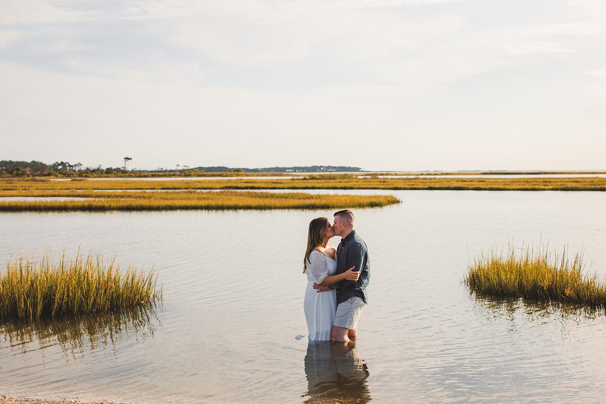 A couple standing ankle deep in still marsh water at golden hour, holding each other