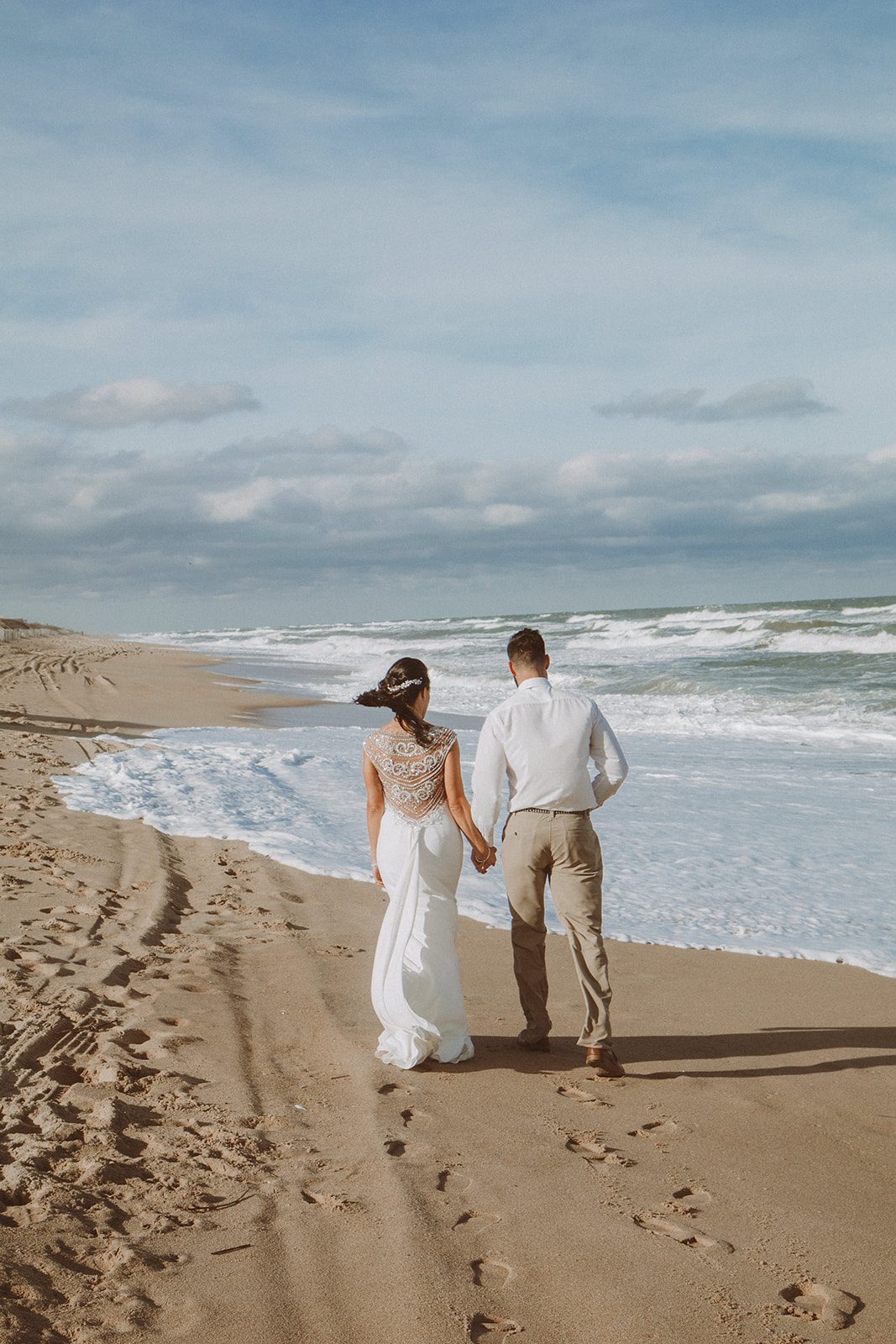 A couple walking hand in hand along the wet sand where the waves are running up the beach