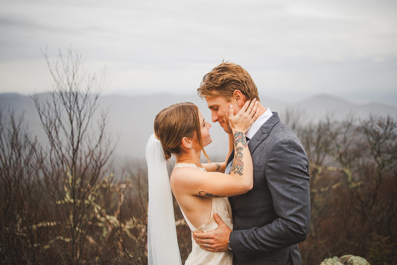 A couple holding each other's faces on a ridge with the Blue Ridge mountains layered behind them